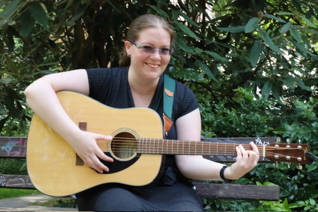 Sarah playing guitar in a park