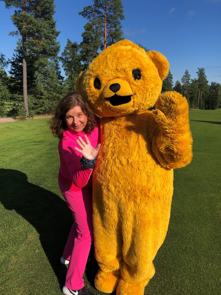 Jaana and Teemu the teddy bear outside on a golf course.